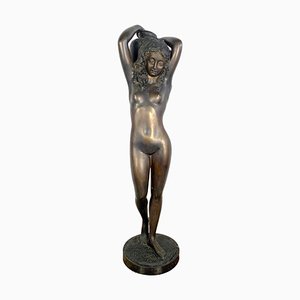 Escultura grande de bronce de una mujer joven desnuda que lleva una urna de agua