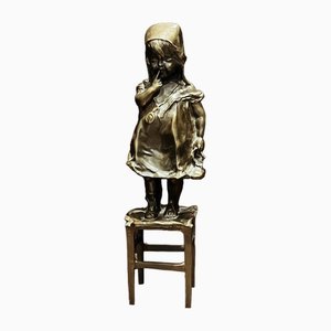 Figura de bronce de una niña de pie sobre una silla