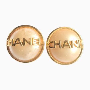Aretes vintage redondos en tono dorado con perla sintética y logo de Chanel. Juego de 2