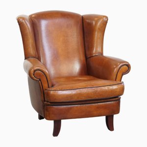 Sillón de orejas de piel de oveja con ribetes negros y formas clásicas