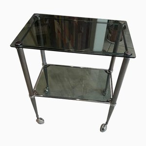 Carrito de bar vintage de metal plateado con dos estantes de vidrio ahumado con ruedas, años 50