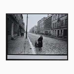 Mujer mayor caminando por la calle con su carretilla de mano de Rolf Gillhausen, años 40